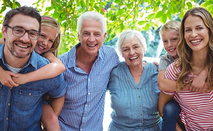 A multigenerational family smiling in front of foliage