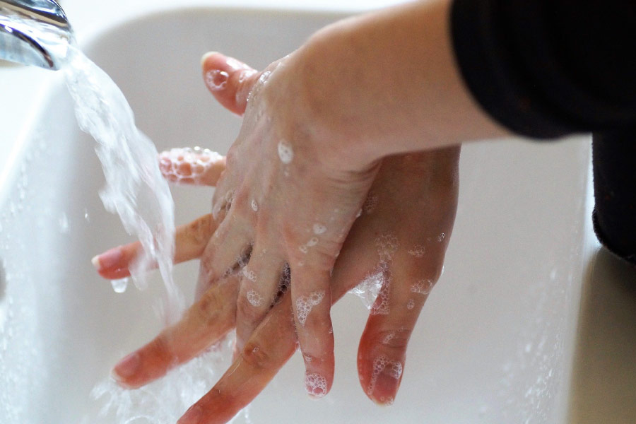 Hands under a running faucet portraying proper hand washing technique 