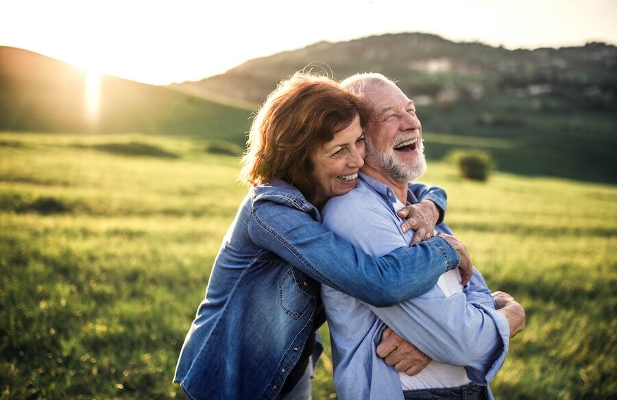 A middle-aged woman and man embrace while smiling outside as the sun sets