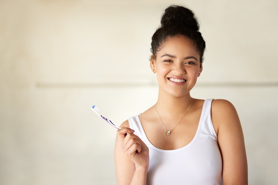 Black young woman smiles while holding a toothbrush to brush her teeth