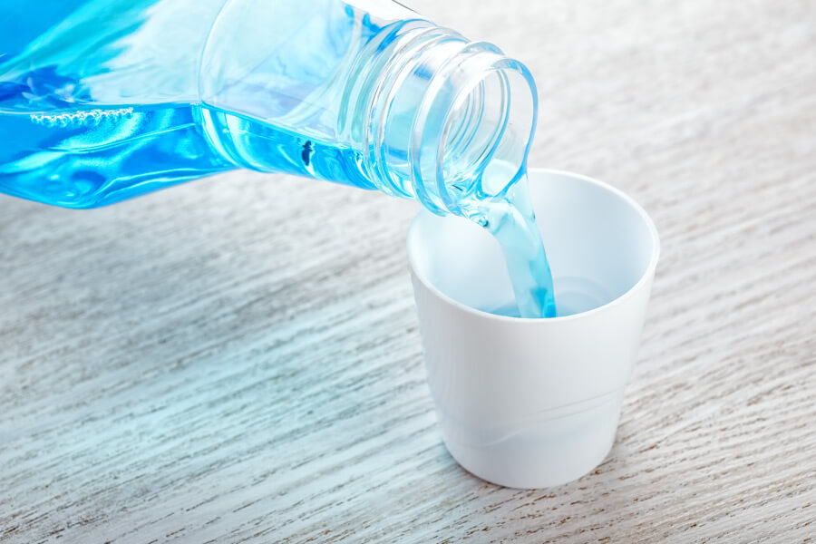 Blue mouthwash being poured from a clear container into a white cup