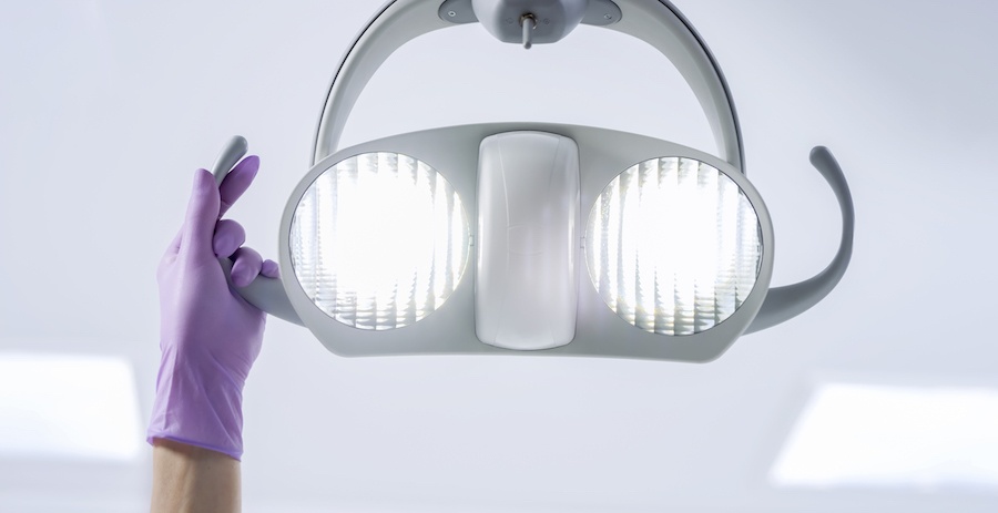 Closeup of a purple gloved hand holding the exam chair overhead lights at a dental office