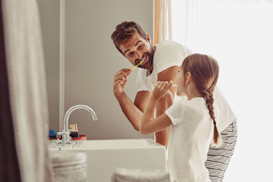 father brushes his teeth with his young daughter at the bathroom sink