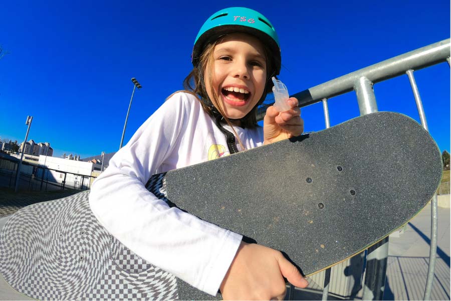 young girl wearing a helmet with a skateboard under her arm hold up her custom mouthguard